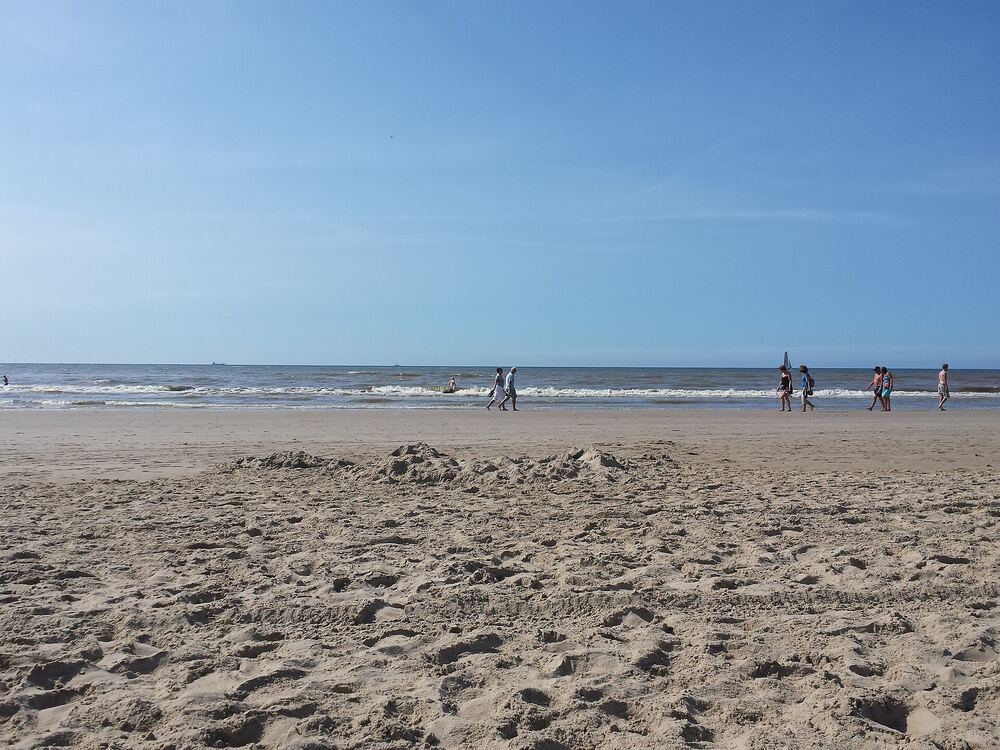 Breed zandstrand met enkele wandelaars aan de waterlijn en de zee op de achtergrond